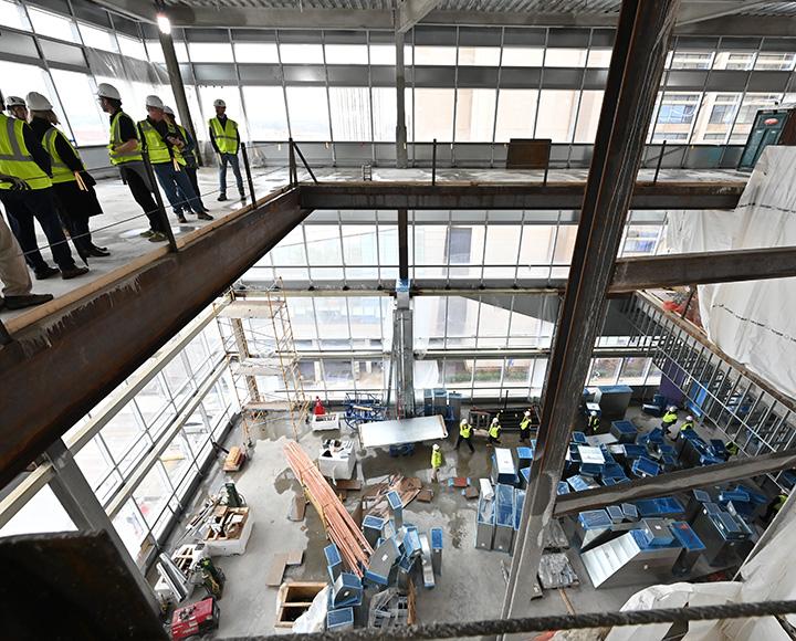 People in neon vests stand on a platform over an unfinished building