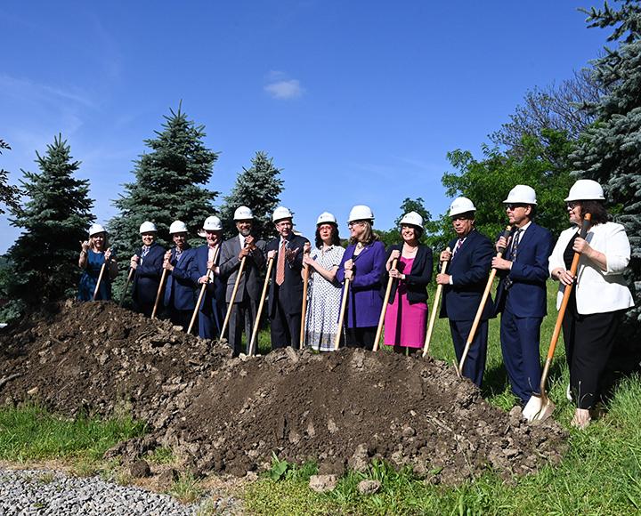 People in hard hats stand before a pile of dirt with shovels