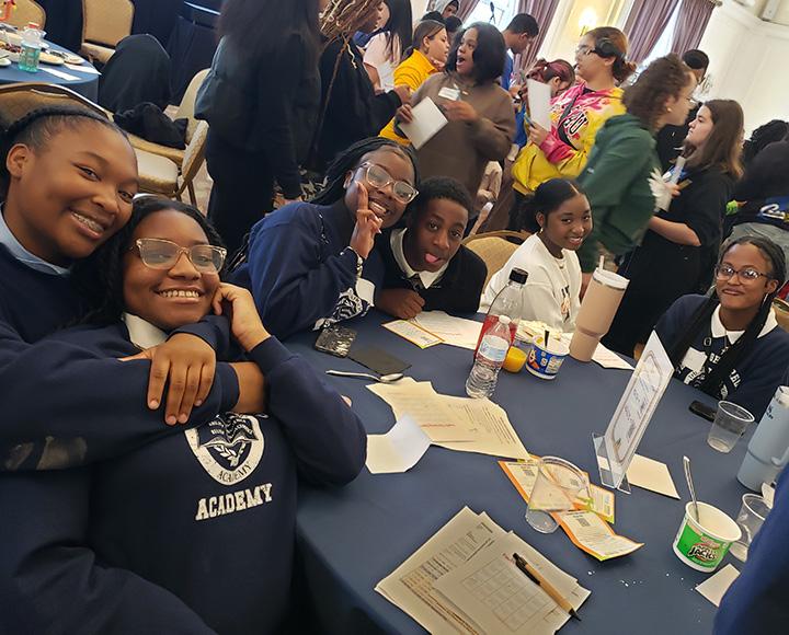Students sitting around a banquet hall table pose