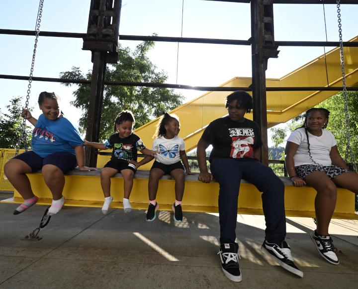 Children sit on a swing made from a yellow-painted girder