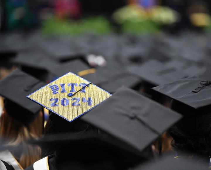 A decorated grad cap reading "Pitt 2024" is visible among the crowd of graduates.