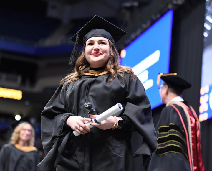 Graduate Lexi Belcufine smiles on stage after collecting her diploma.