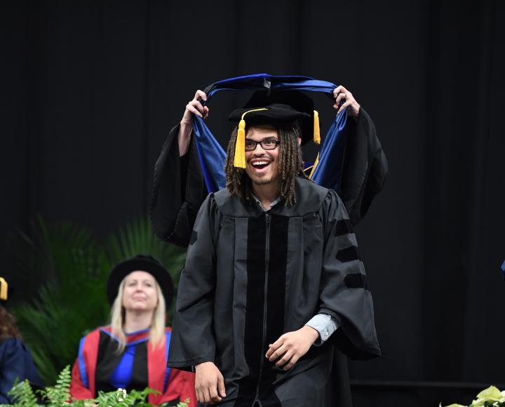A student smiles while receiving their regalia on stage.