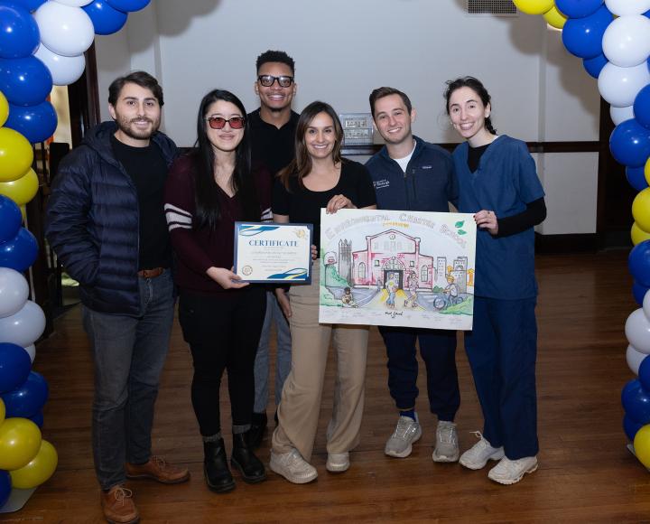 A group holds up a certificate and drawing of a building under a balloon arch