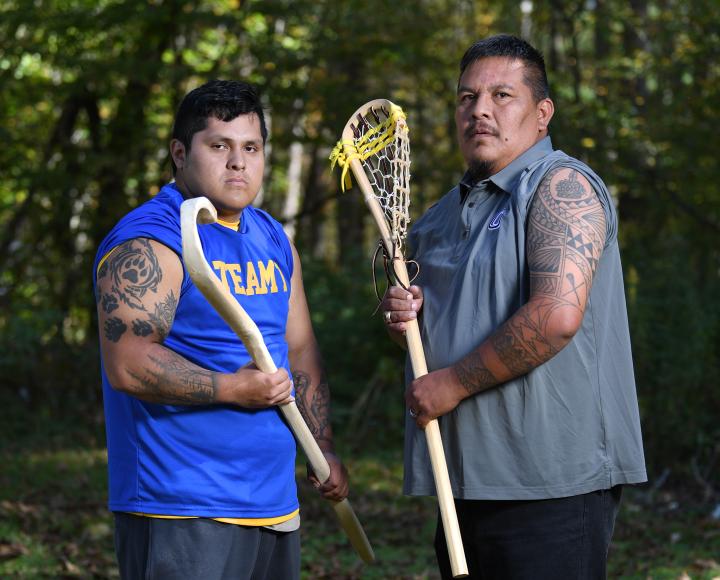 Two men posting with lacrosse sticks in front of wooded background