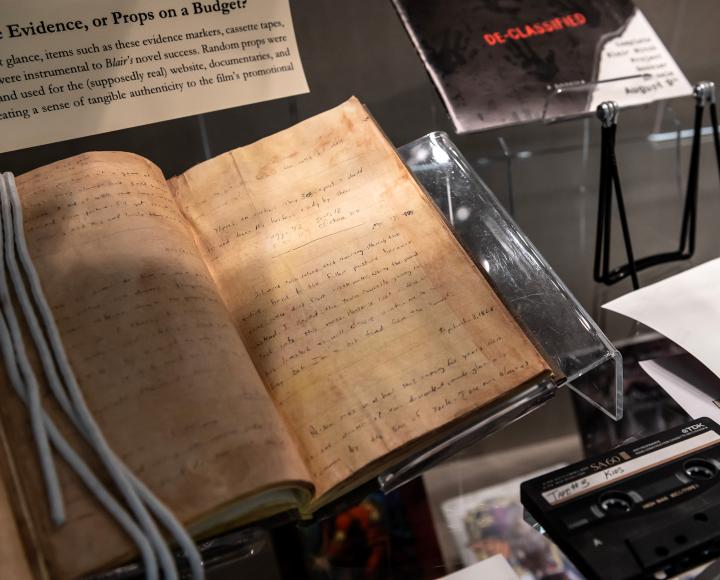 A journal, cassette tapes and other props in a glass display case.