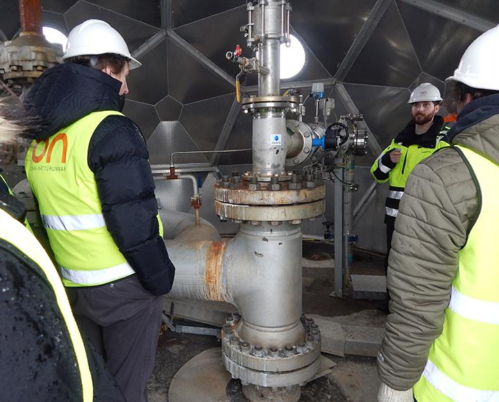 People in florescent vests look at large industrial pipes inside the dome.
