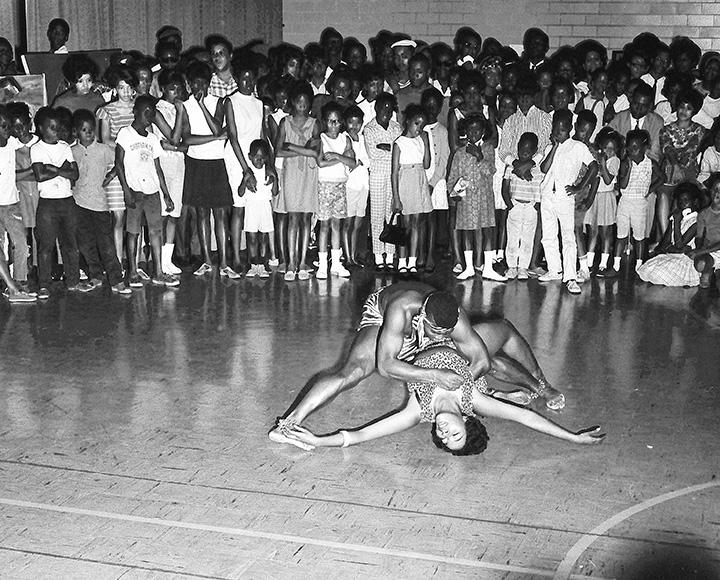 A crowd watches two dancers on the floor of a gymnasium