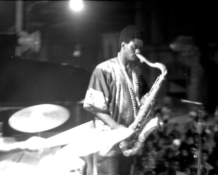 A blurry black and white photo of a saxophonist on stage.