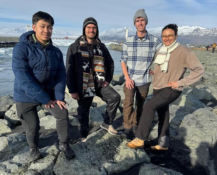 Four people pose on rocks by the sea.