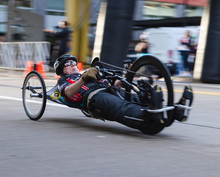 A hand cyclist speeds down a street.