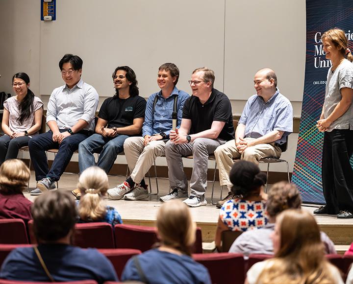 The panel of researchers sit on chairs on a stage