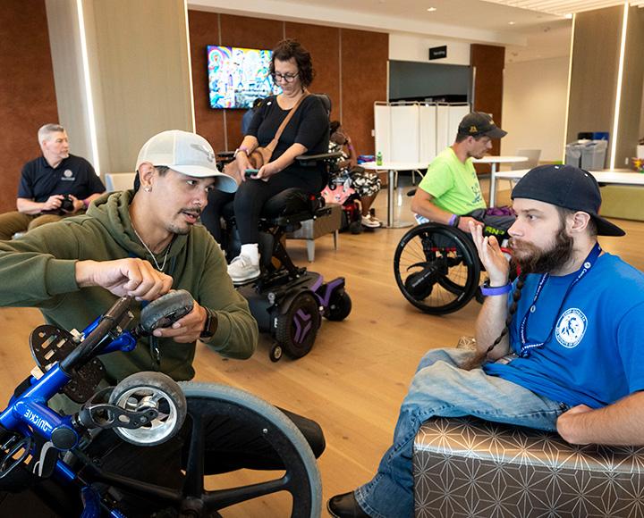 A person chats with another person as he tightens a wheel on a wheelchair.