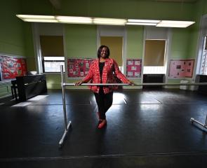 Woman stands in studio with her hands on a ballet barre.