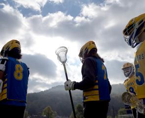 Lacrosse players silhouetted against cloudy skies and mountains