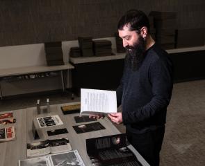 Ben Rubin, Horror Studies Collection Coordinator at the University Library System, stands in a darkly lit room before a table of newly acquired Blair With Project items in the Special Collections section of the Hillman Library. Items include film posters, props, pamphlets and more.