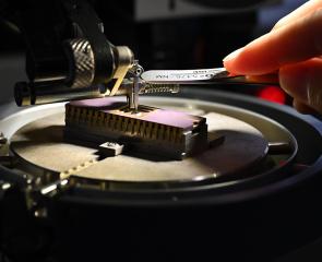 A hand uses a tool to adjust a small device