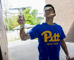 Man with blue Pitt shirt cleaning window from the outside