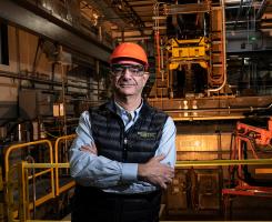 Carniero, wearing an orange hardhat, stands in an industrial factory