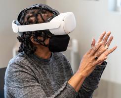 A person wearing a VR headset holds up their hands and speaks to an instructor