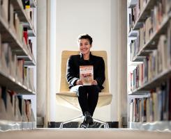 Roberts holds her book at the end of two library stacks