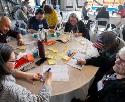 People sit at circular tables, taking notes in small groups