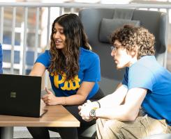 Four students huddle around a laptop