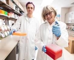 Zak Hutchinson and Anna Marsland in white lab coats, holding pipette tip boxes.