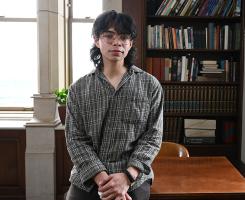 Diaz leans on a table near a bookshelf