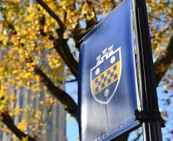 Banner with Pitt shield flies in front of fall leaves and Cathedral of Learning.