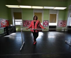 Woman stands in studio with her hands on a ballet barre.