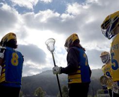 Lacrosse players silhouetted against cloudy skies and mountains