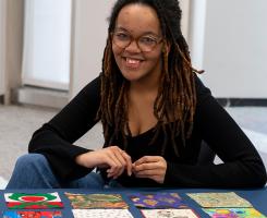 Maria McDill sits at a table where quilt squares are laid out in front of her