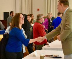 A woman and man shaking hands over a table at an event.