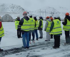 A group of students stand in florescent vests on a snowy plain.