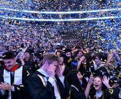 Students at graduation cheering as blue and gold confetti falls