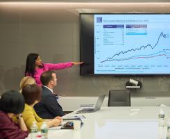 Woman gives presentation in boardroom, pointing to chart showing business growth