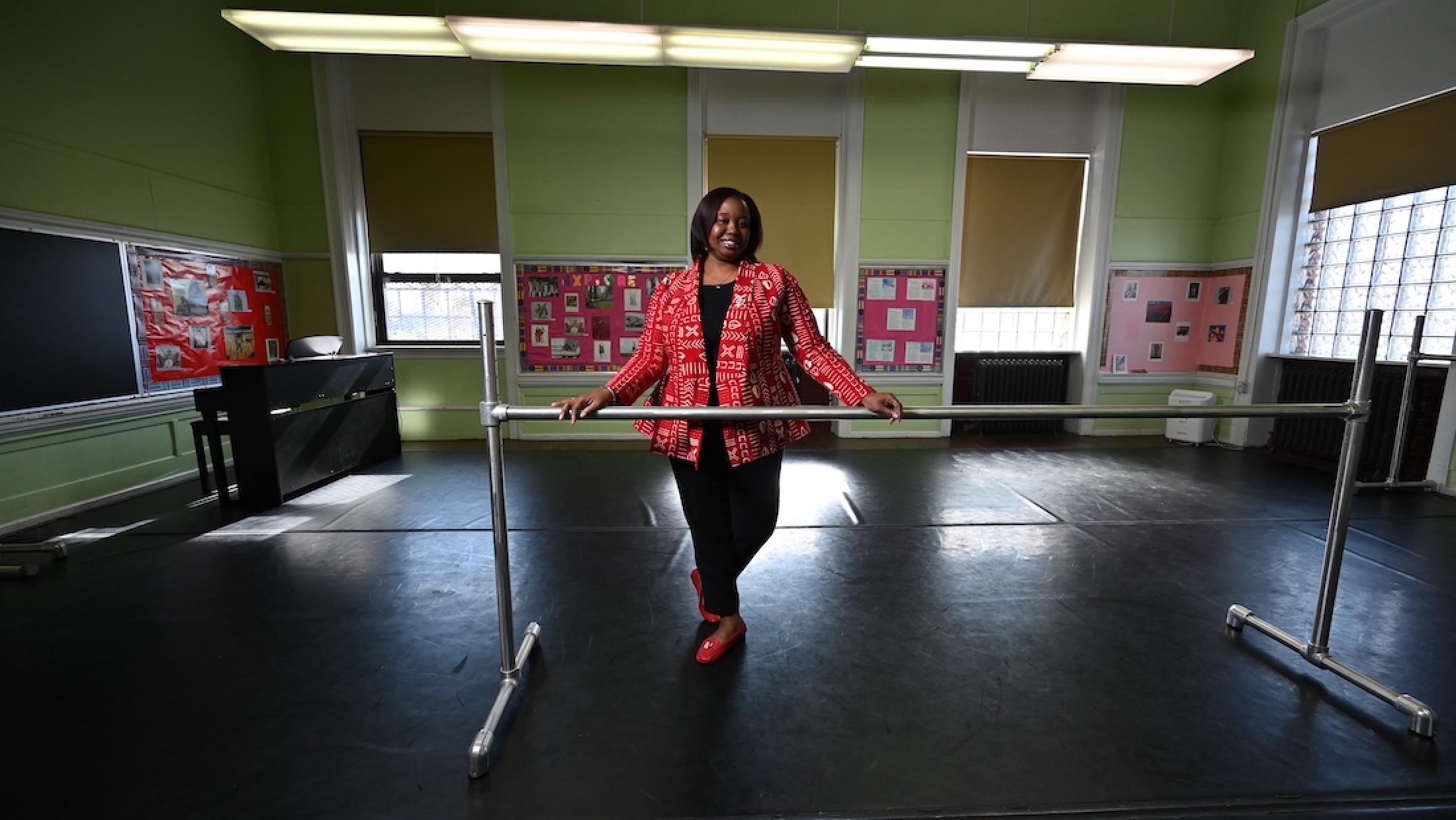 Woman stands in studio with her hands on a ballet barre.