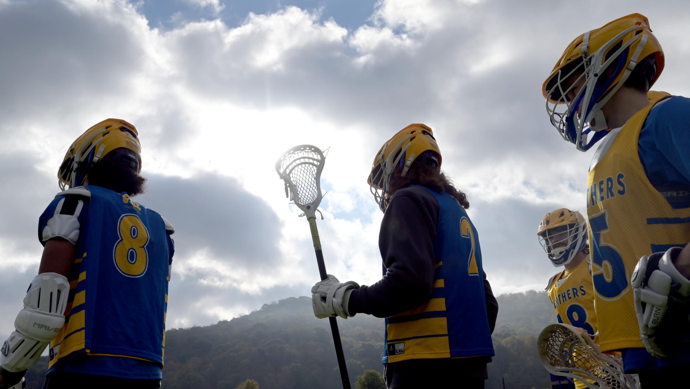 Lacrosse players silhouetted against cloudy skies and mountains