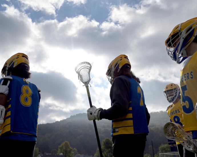 Lacrosse players silhouetted against cloudy skies and mountains