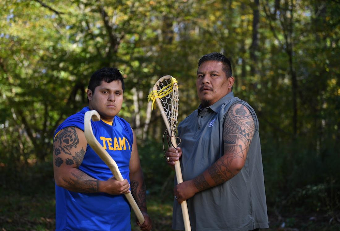 Two tattooed men holding wooden lacrosse sticks