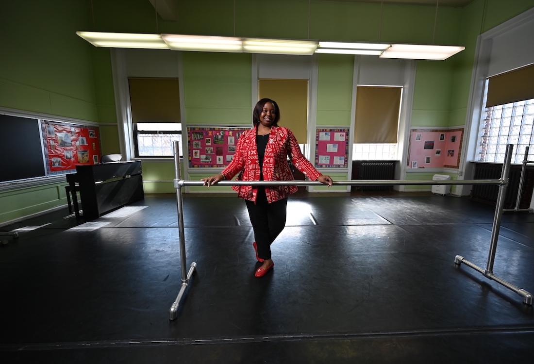A woman stands in a studio with her hands on a ballet barre.