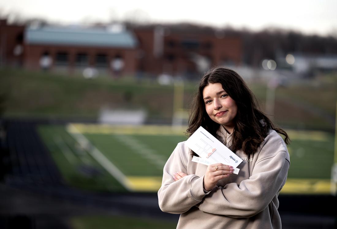 A 14-year-old girl holds a National Marrow Donor Program swab kit while posing for a photo on a school campus