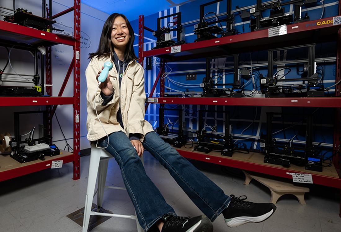 Woman sitting on stool posing for photo in lab holding medical device