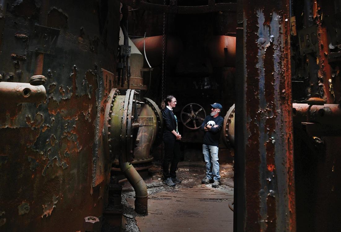 Woman and man standing inside a rusted industrial machine.