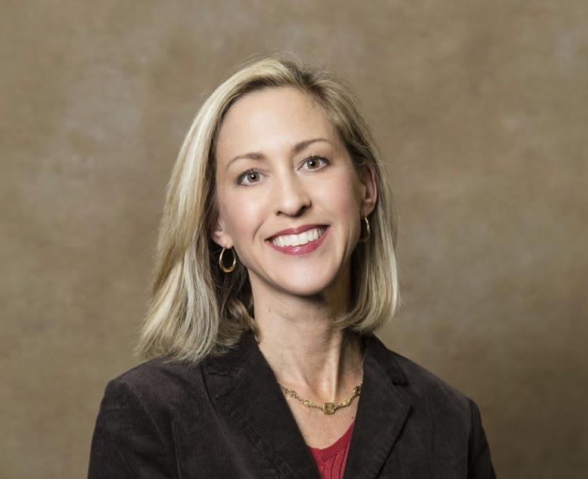 a person in a dark blazer in front of a tan photography background