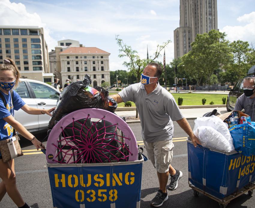 three people dragging blue and gold housing carts through Oakland
