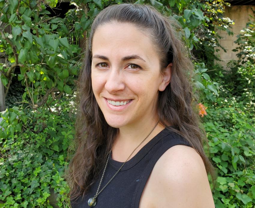 a woman in a dark tank top standing in front of trees