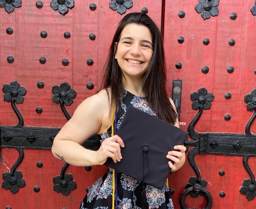 a woman in a black patterned dress holding a mortarboard in front of a black and red door