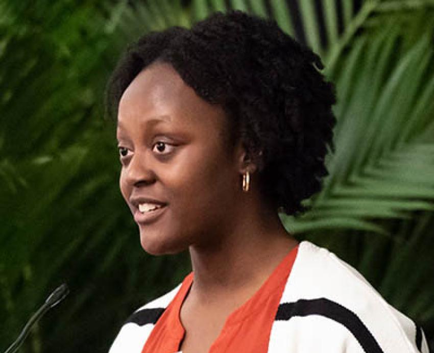 Fodun Ologunde in an orange shirt and black and white jacket stands at a podium